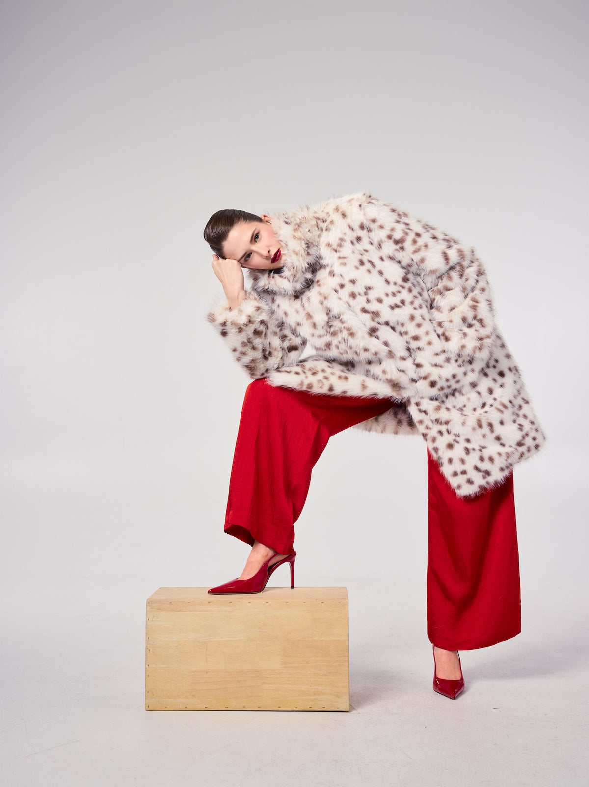 AUDREY jacket in Java Bean — model wearing a long vegan faux fur jacket with a spotted pattern, styled with bold red tailoring and pointed heels for a striking editorial look.