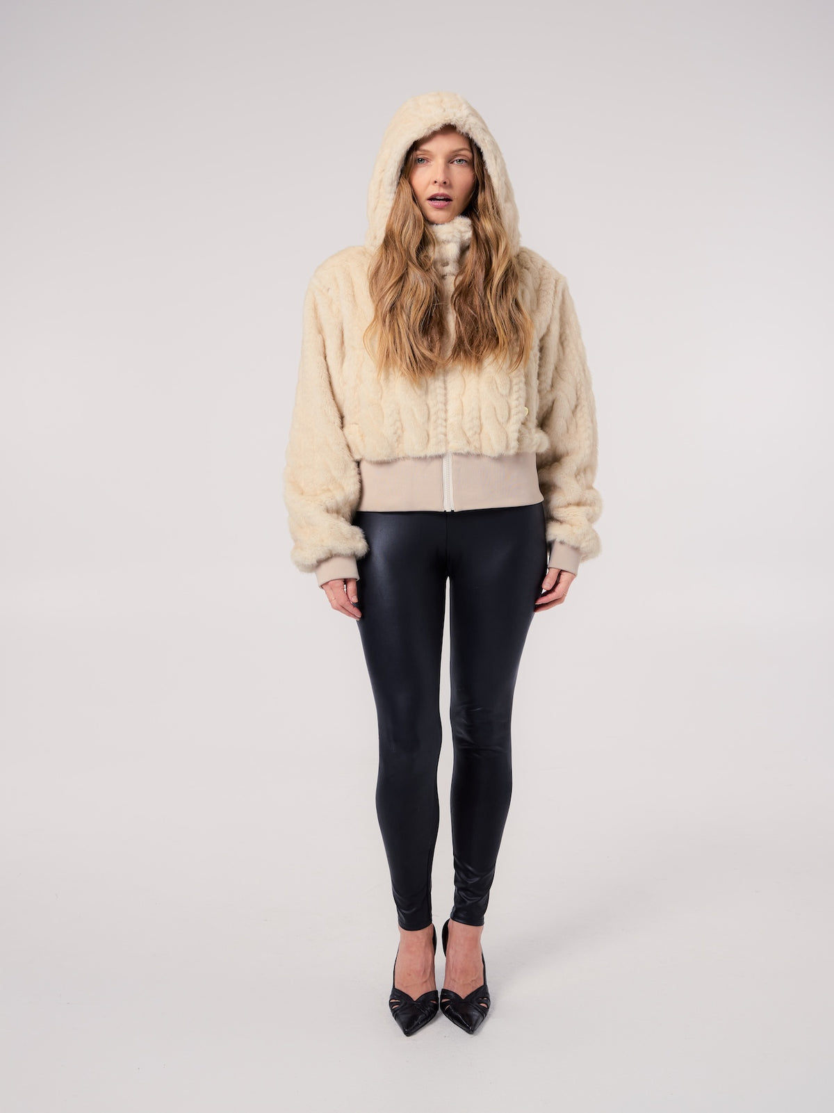 FIONA jacket in Cream Cable — model wearing a hooded vegan faux fur jacket with a cable-inspired textured finish, styled with sleek black leggings for a modern cold-weather look.