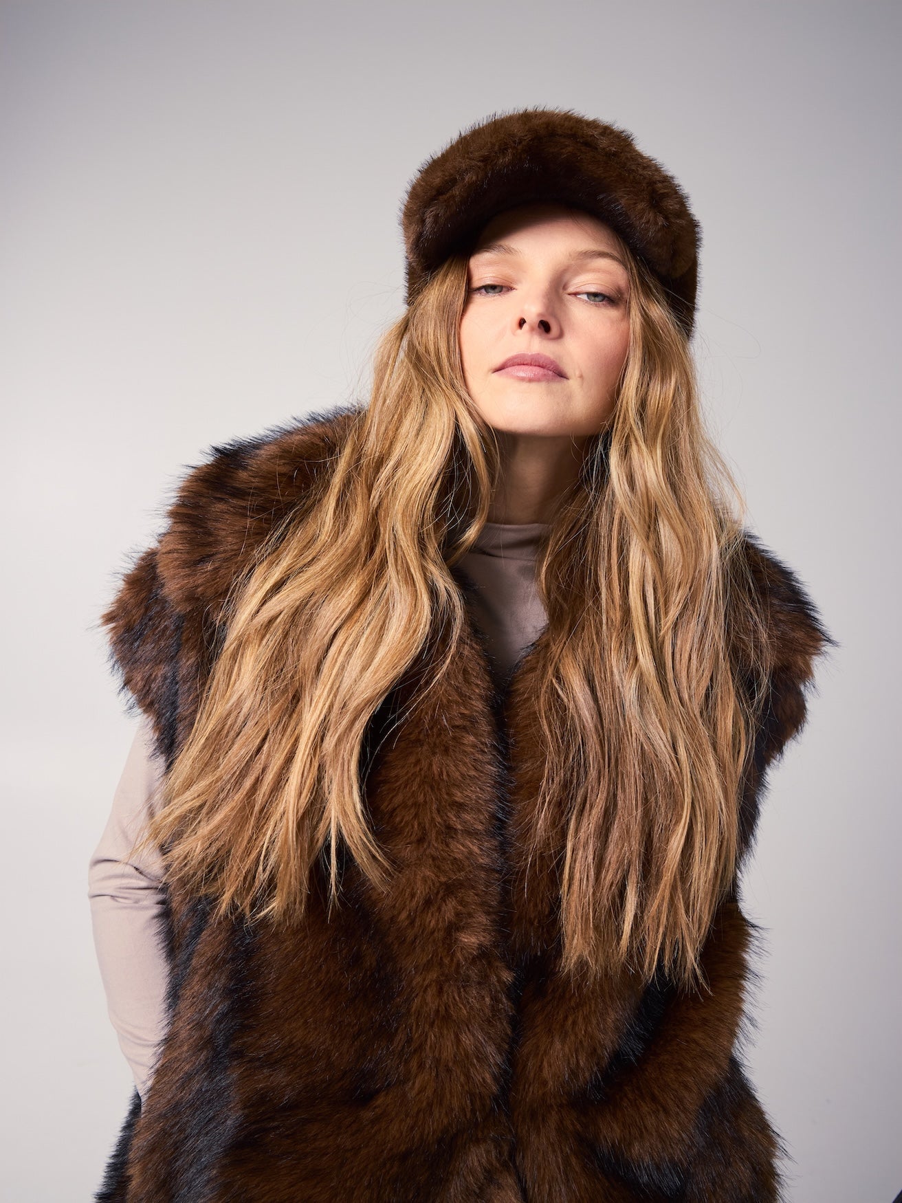 MIA vest in Grizzly — model wearing a vegan faux fur vest with rich brown tones, styled with a matching faux fur cap for a sophisticated cold-weather editorial look.