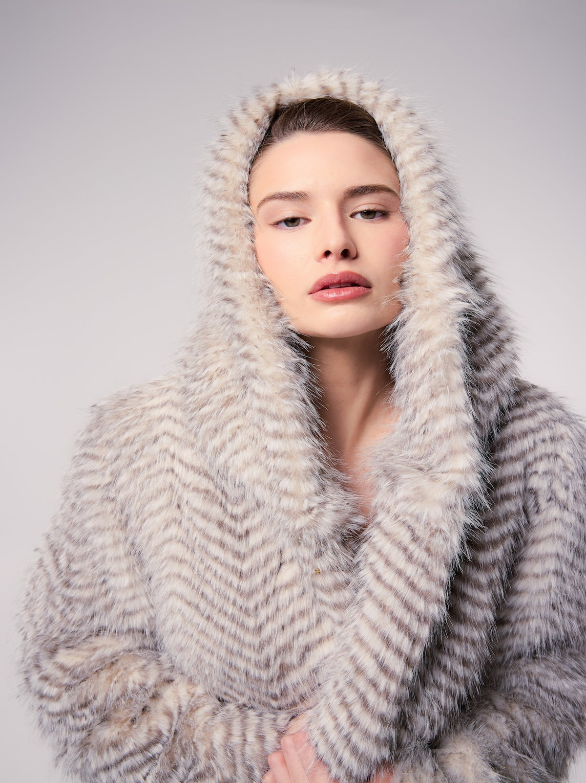 NIKKI jacket in Snow Lynx — model wearing a hooded vegan faux fur jacket with a striped Snow Lynx pattern, creating a soft, luxurious cold-weather editorial look.