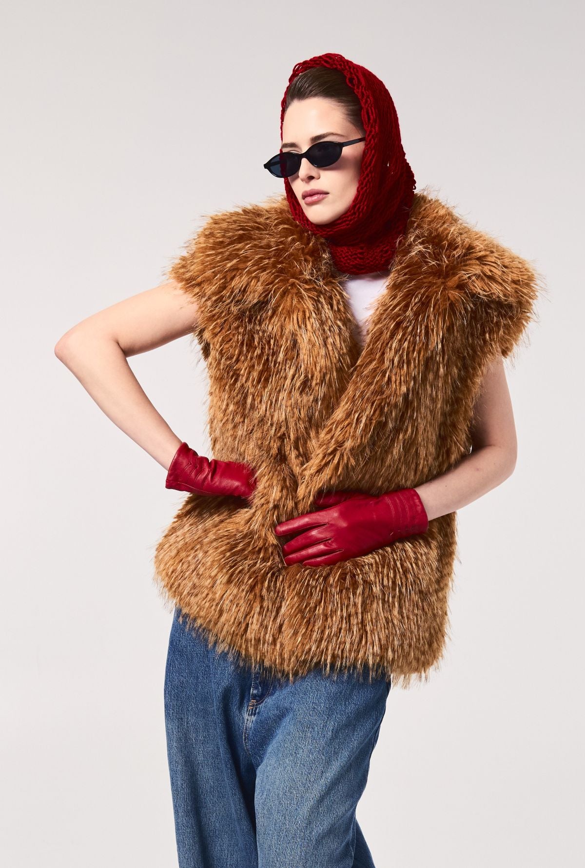 Model wearing the FREED Mia Butterscotch faux fur vest styled with red gloves, a red knit scarf, sunglasses, and jeans.