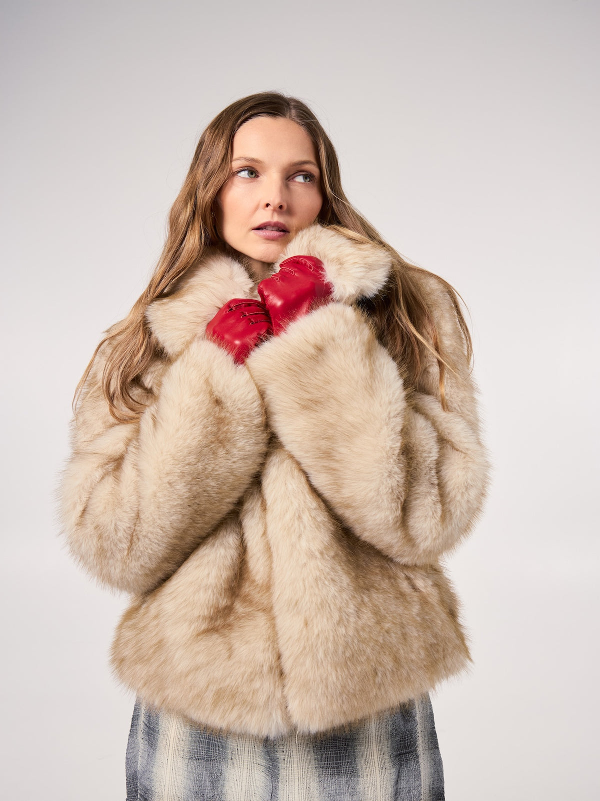CORI jacket in Fox — model wearing a vegan faux fur jacket with a soft natural-tone finish, styled with red leather gloves for an elegant cold-weather editorial look.
