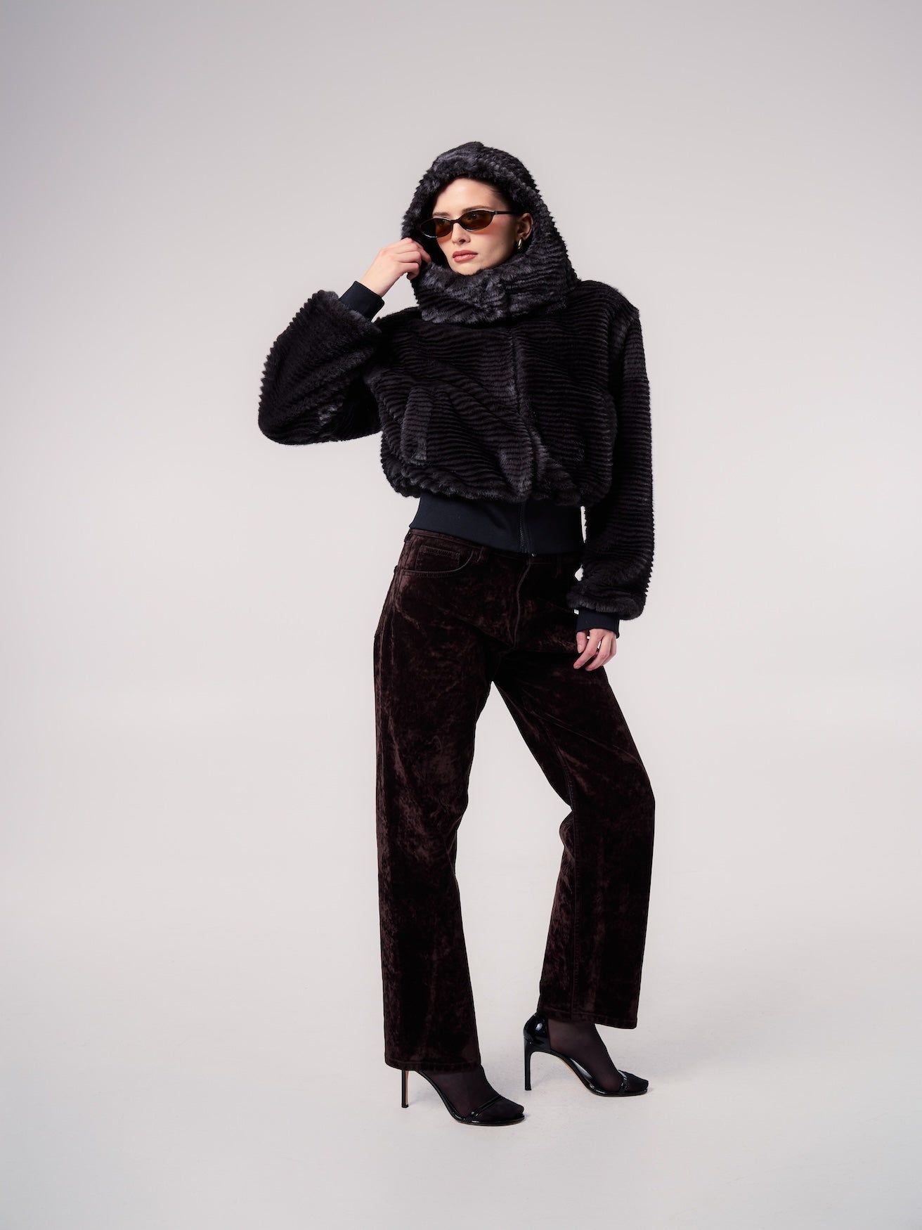 FIONA jacket in Shadow Stripe — model wearing a hooded vegan faux fur jacket with a textured striped finish, styled with oversized sunglasses and tailored trousers for a sophisticated cold-weather look.
