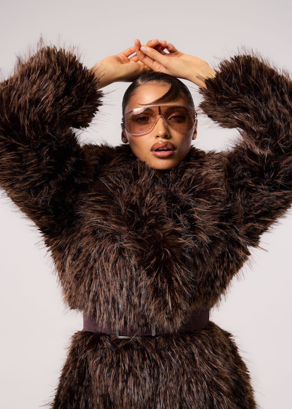 LONDON coat in Sable — model wearing a belted vegan faux fur coat with a rich sable finish, styled with oversized tinted sunglasses for a bold luxury editorial look
