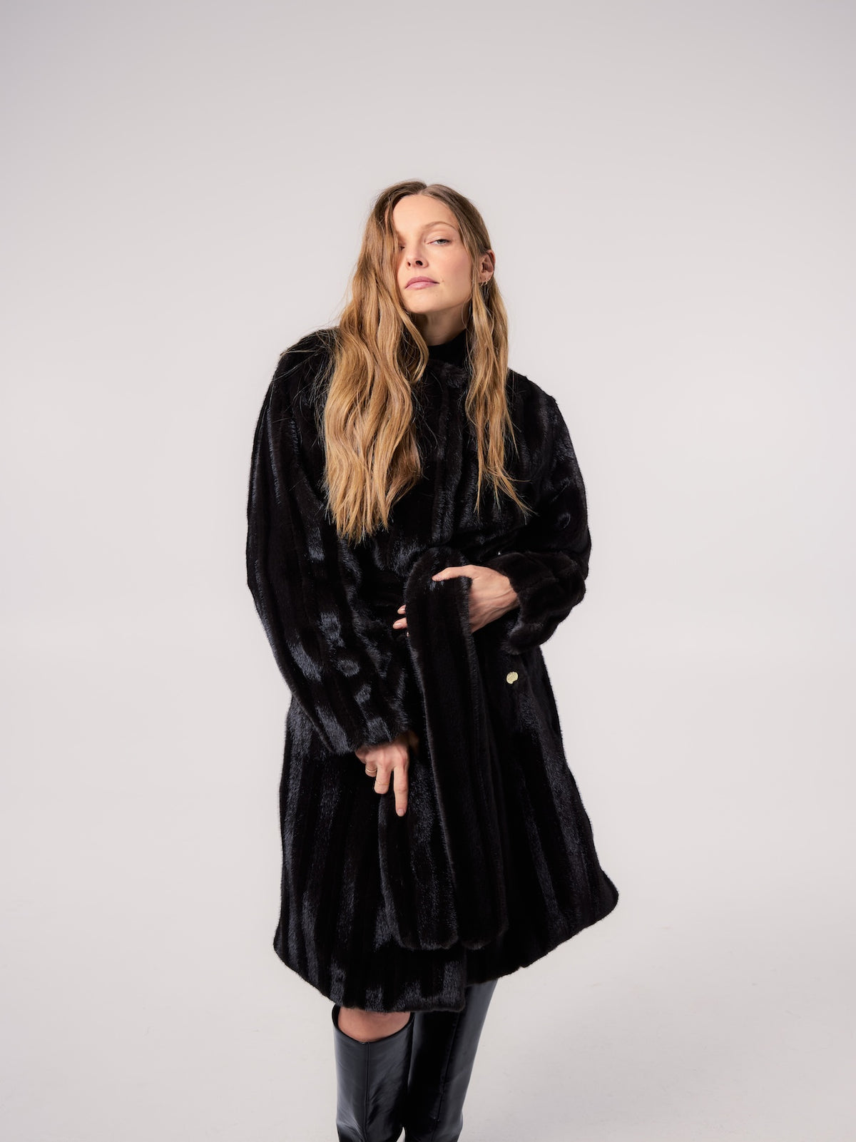 STELLA jacket in Black Stripe — model wearing a vegan faux fur jacket with a sleek striped texture, styled with knee-high boots for a sophisticated cold-weather editorial look.