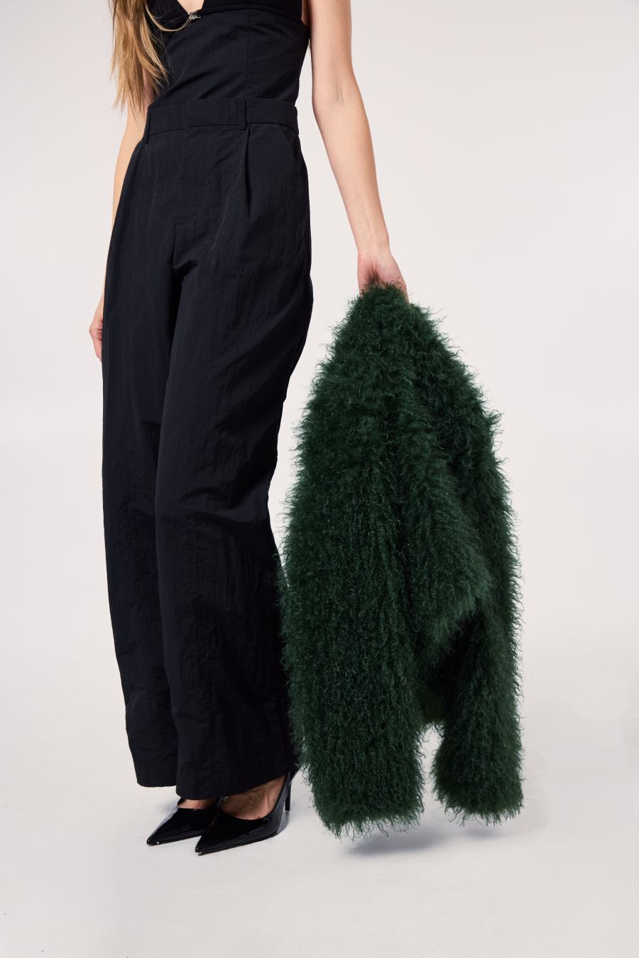 Model holding a rich evergreen faux fur coat against a clean studio backdrop, paired with an all-black look.